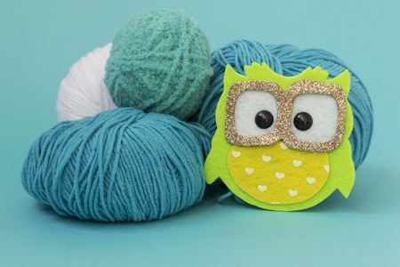 Self-made soft toy owl made of felt, on a color monophonic background. The owl stands next to the balls of yarn. There is a place for text. Hobby conceptの写真素材