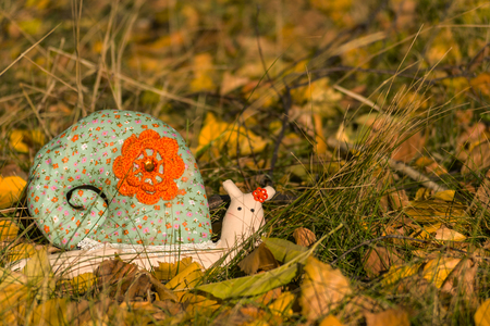 Textile toy snail crawling on the yellow foliage and grass. Close-up. Blurred background. There is a place for text.の写真素材