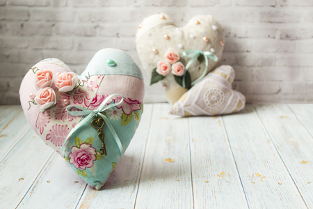 Three textile hearts with a romantic flower color on a simple light wooden background. selective focus. There is a place for text. Shabby chic style.の写真素材