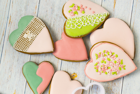 Pink and colored gingerbread and honey cakes and heart-shaped cookies lie in a messy pile on a light wooden background. Nearby are white molds for baking. Place for text. The concept of love, mother's day, cooking, Valentine's Day.の写真素材