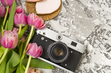 The old camera is lying on a concrete table, next to a pink cookie, next to it are a pink bouquet of tulip flowers. Concept breakfast, There is a place for text.の写真素材