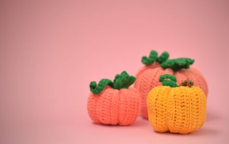 Autumn pink background with knitted pumpkins. Side view of knitted pumpkins of different sizes. Happy Thanksgiving Autumn Background. Autumn concept, there is a place for text.の写真素材