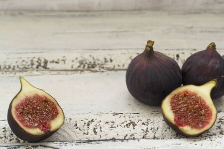 Three fresh figs on a wooden white table. One fig is cut in halves and its flesh is visible. Located in a group. The concept of urge.の写真素材