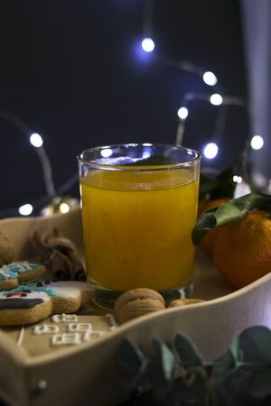 Gingerbread Christmas cookies in the shape of a house, a snowman and stars lie on a spacing with fresh orange juice in a glass of drink in a farm style. Around are nuts, cinnamon, decor. Blurred background with garlands. Table setting breakfast for the New Year.の写真素材