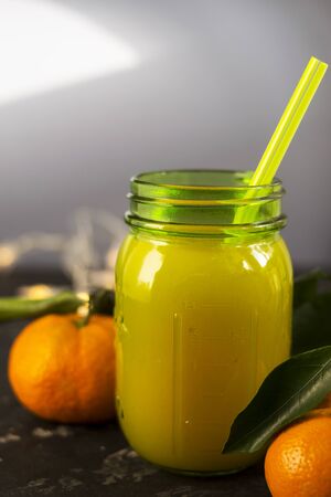 Freshly squeezed orange juice in a mason jar and fresh oranges fruit with green wet leaves on a black shabby background. Healthy lifestyle concept.の写真素材