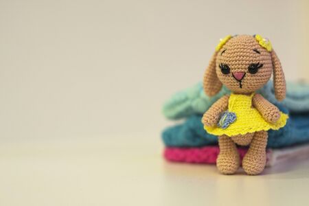 Knitted doll hare and knitted in yellow clothes - colored toy amigurumi on a light background. Copy space. Hobby and needlework concept.の写真素材