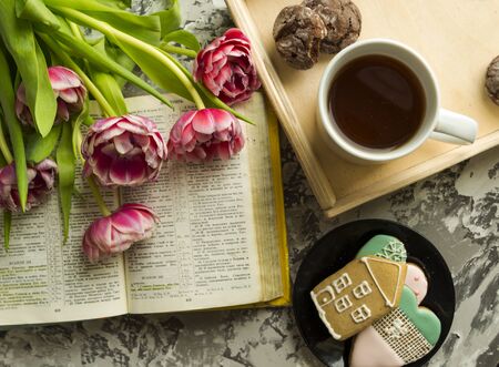 Breakfast on March 8 with pink tulips, a cup of tea, a book and macaroons on a concrete background....