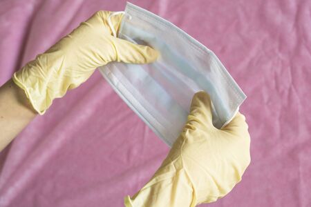 A man holds a medical mask in two hands. Hands in medical gloves. Pink background. Health and medicine concept.の写真素材