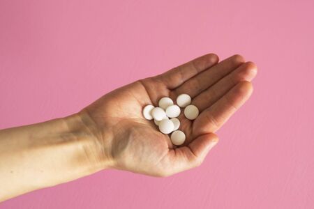 White closeup tablets on a woman's hand. Pink background. Concept - medicine, recovery of a sick...