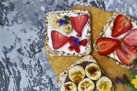 Breakfast with toaster and oat bread, buttered with butter, jam, strawberries and bananas on a concrete table. Useful summer food concept.の写真素材