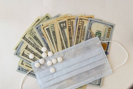 Pills, protective mask, medical supplies and dollar bills on a white background. The concept of expensive medicine. Pharmaceutical industry and health insurance. There is a place for text.の写真素材