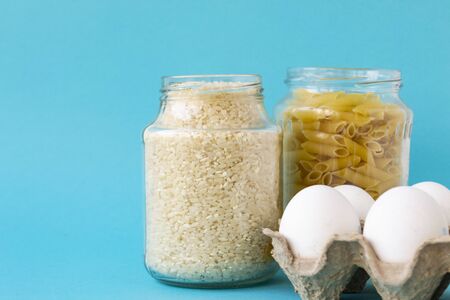 Noodles, rice, pasta in jars and eggs lie on a blue background. Raw food for cooking. There is a...
