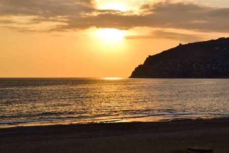 Golden sunset over the Mediterranean Sea. The setting sun shines through the clouds, and a golden path is visible above the ocean. Silhouetted mountains on the horizon. Beach resortの写真素材