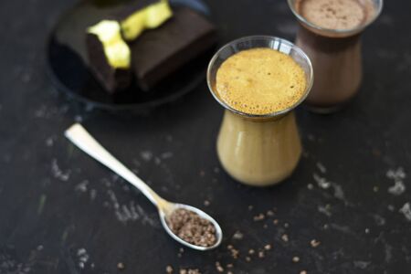 Dalgona coffee and cocoa in glass transparent glasses. Nearby lies a metal spoon with instant coffee, and a chocolate dessert on a saucer. Black backgroundの写真素材