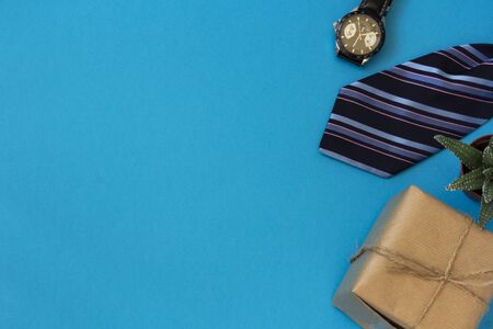 Happy fathers day gift layout on a blue background. Greeting card with a side border of gifts, ties and a wristwatch, a green flower of a succulent in a pot in a layout. Top view with copy space.の写真素材