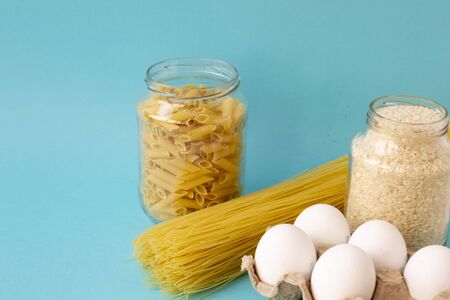 Noodles, rice, pasta in jars and eggs lie on a blue background. Raw food for cooking. There is a place for text.の写真素材