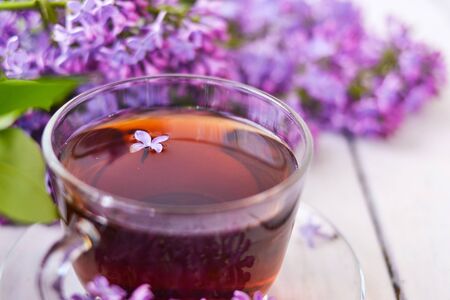 Cup of tea with lilac flowers on a wooden white background. Mocap for postcards. Spring time. Vase with lilacs. Copy space for text. The concept of holidays and good morning wishes.の写真素材