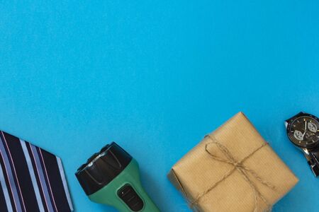 Happy fathers day. Flat layout with congratulations. On a blue background are a striped tie, a flashlight, a box in kraft paper, a watch.の写真素材