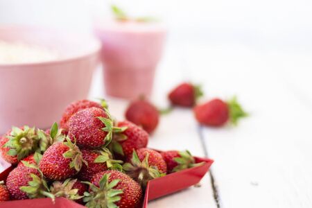 Fresh strawberry yogurt with berries around on a white wooden background. A pink shake in a glass, next to it is a pink cup with Hercules flakes, and red strawberries lie in a red star-shaped plate.の写真素材