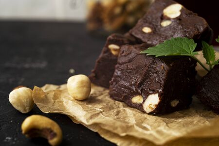 Fondant on craft crumpled paper with nuts and chocolate cubes decorated with green mint leaves. In the background a jar of nuts, blurred background. Sweet composition on a black textural background. Copy space.の写真素材