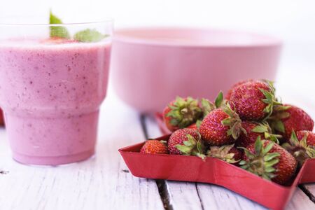 Fresh strawberry yogurt with berries around on a white wooden background. A pink shake in a glass, next to it is a pink cup with Hercules flakes, and red strawberries lie in a red star-shaped plate.の写真素材