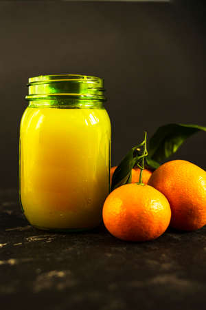 Fresh tangerine juice in a glass jar on a black background. Whole tangerines with green leaves lie nearby. Healthy eating concept.の写真素材