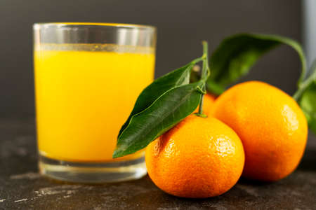 Fresh tangerine juice in a glass cup on a black background. Whole tangerines with green leaves lie nearby. Healthy eating concept.の写真素材