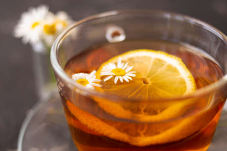 A cup of flower tea with lemon and pharmacy chamomile. Black blurred background. Close shot.の写真素材