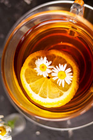 A cup of flower tea with lemon and pharmacy chamomile. Black blurred background. Close shot.の写真素材