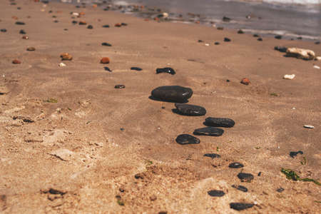 Black flat zen stones lie on the sand of a sea beach.の写真素材