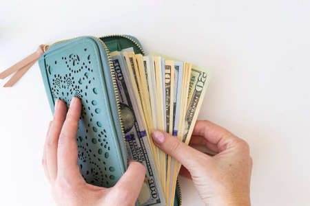 Buying for dollars. A woman's hand holds a green wallet and counts out money. White background.