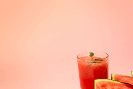 Delicious red watermelon juice with sliced fruit pieces on a plate. A sprig of mint in a glass. Copy...
