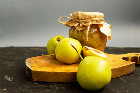 Pear jam in a glass jar. The jar is covered with craft paper and tied with a jute rope. Sweet jam stands on a cutting board and fresh yellow pear fruits lie nearby.の写真素材