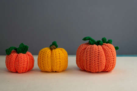 Autumn composition of three pumpkins, knitted decor of orange and yellow pumpkins on a gray background, yarn and needlework, soft light.の写真素材