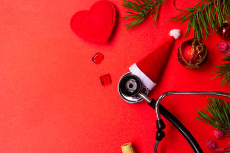 Medical Christmas banner with pills, stethoscope, test tubes, gift box, Santa hat, Christmas toys, heart, and a Christmas tree on a red background. Copyspace. The new year's cure is categorical. Christmas medical flatly.の写真素材
