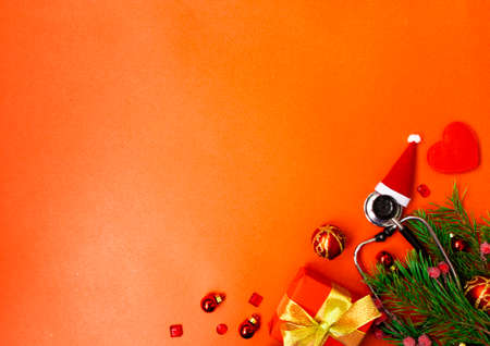 Christmas banner with a Phonendoscope wearing a Santa Claus hat. Nearby lie red balls, a heart, a gift box, branches of a Christmas tree. Medical banner concept for New Year. The colors are red and gold.の写真素材