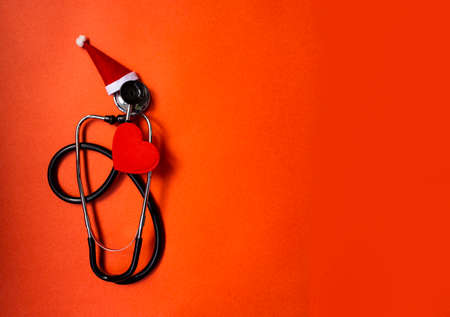 Christmas banner with Phonendoscope, which is decorated with Santa Claus hat. Nearby are red hearts. Medical banner concept for New Year. The colors are red and gold.の写真素材