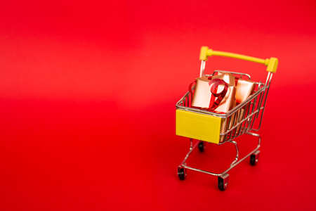Grocery basket with golden gift boxes with red ribbon on red background banner with copy space. Christmas shopping online. Winter holiday sales, seasonal sales, Black Friday, Christmas, discounts and online shopping. Xmas sale.の写真素材