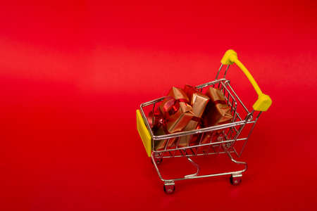 Grocery basket with golden gift boxes with red ribbon on red background banner with copy space. Christmas shopping online. Winter holiday sales, seasonal sales, Black Friday, Christmas, discounts and online shopping. Xmas sale.の写真素材
