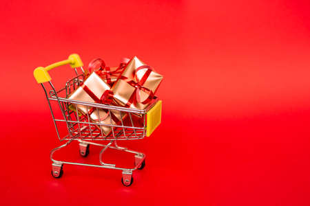 Grocery basket with golden gift boxes with red ribbon on red background banner with copy space. Christmas shopping online. Winter holiday sales, seasonal sales, Black Friday, Christmas, discounts and online shopping. Xmas sale.の写真素材