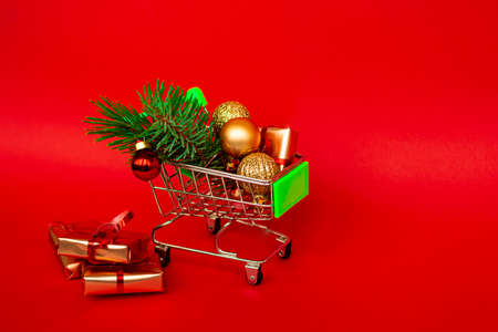 Grocery basket with golden gift boxes and christmas balls, sprig of christmas tree on red banner background with copy space. Xmas sale .. Christmas shopping online. Winter holiday sales and discounts, seasonal sales, Black Friday, Christmas, discounts and online shopping.の写真素材