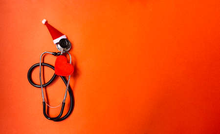 Christmas banner with Phonendoscope, which is decorated with Santa Claus hat. Nearby are red hearts. Medical banner concept for New Year. The colors are red and gold.の写真素材