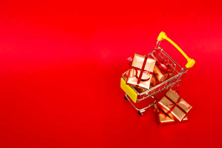Grocery basket with golden gift boxes with red ribbon on red background banner with copy space. Christmas shopping online. Winter holiday sales, seasonal sales, Black Friday, Christmas, discounts and online shopping. Xmas sale.の写真素材