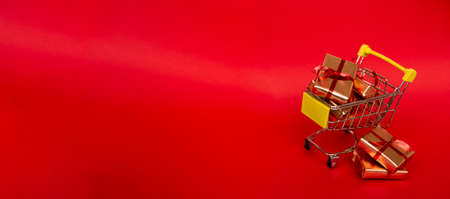 Grocery basket with golden gift boxes with red ribbon on red background banner with copy space. Christmas shopping online. Winter holiday sales, seasonal sales, Black Friday, Christmas, discounts and online shopping. Xmas sale.の写真素材