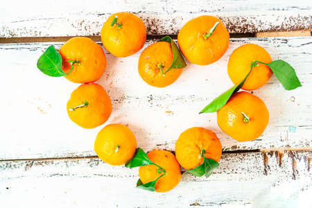 Small tangerines are laid out in the shape of a heart and lie on a white wooden table. Healthy food concept.の写真素材