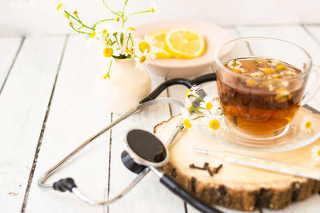 Decoction of chamomile, dried flower in flower tea and a phonendoscope, sliced lemon on a white wooden background. Health concept, prostate treatment, doctor prescribing treatment.の写真素材