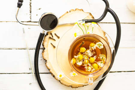 Decoction of chamomile, dried flower in flower tea and a phonendoscope, sliced lemon on a white wooden background. Health concept, prostate treatment, doctor prescribing treatment.の写真素材