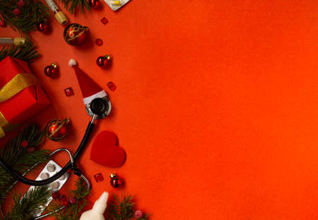 Christmas banner with a Phonendoscope wearing a Santa Claus hat. Nearby lie red balls, a heart, a gift box, branches of a Christmas tree, pills, and medical test tubes. Medical banner concept for New Year. flatly. The colors are red and gold.の写真素材