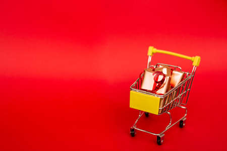 Grocery basket with golden gift boxes with red ribbon on red background banner with copy space. Christmas shopping online. Winter holiday sales, seasonal sales, Black Friday, Christmas, discounts and online shopping. Xmas sale.の写真素材