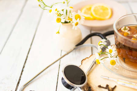 Decoction of chamomile, dried flower in flower tea and a phonendoscope, sliced lemon on a white wooden background. Health concept, prostate treatment, doctor prescribing treatment.の写真素材